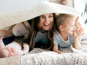 Happy mommy plays with the children on the bed and covers the children and herself with a blanket.